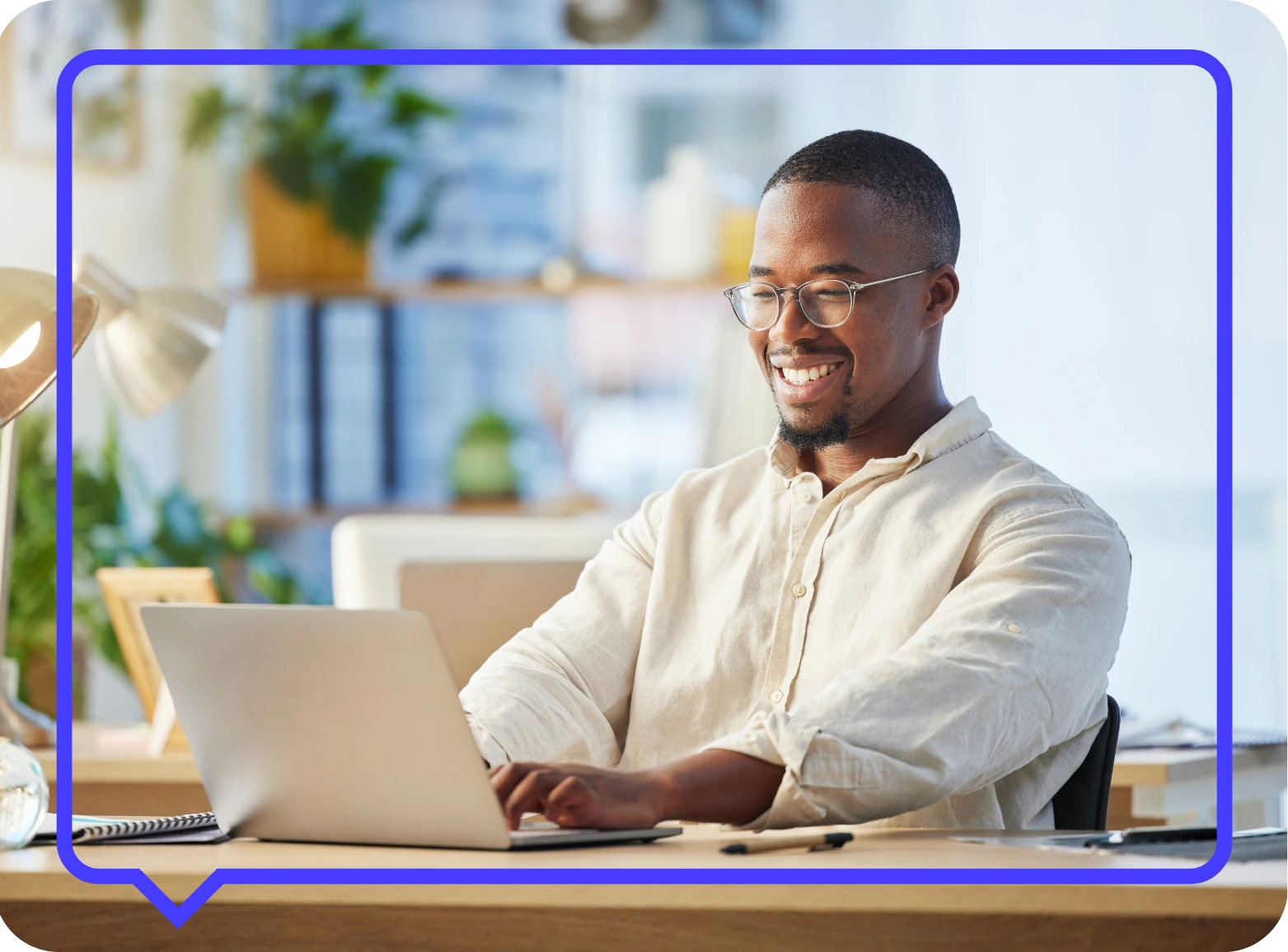 An man smiling sat at his desk working on a laptop in an office.