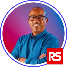 Smiling man in glasses and blue shirt with RS Group logo in the corner, shown in a circular frame on a red and purple gradient background